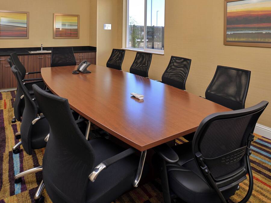 A conference room with a large wooden table, black chairs, a telephone, and artwork on the walls.