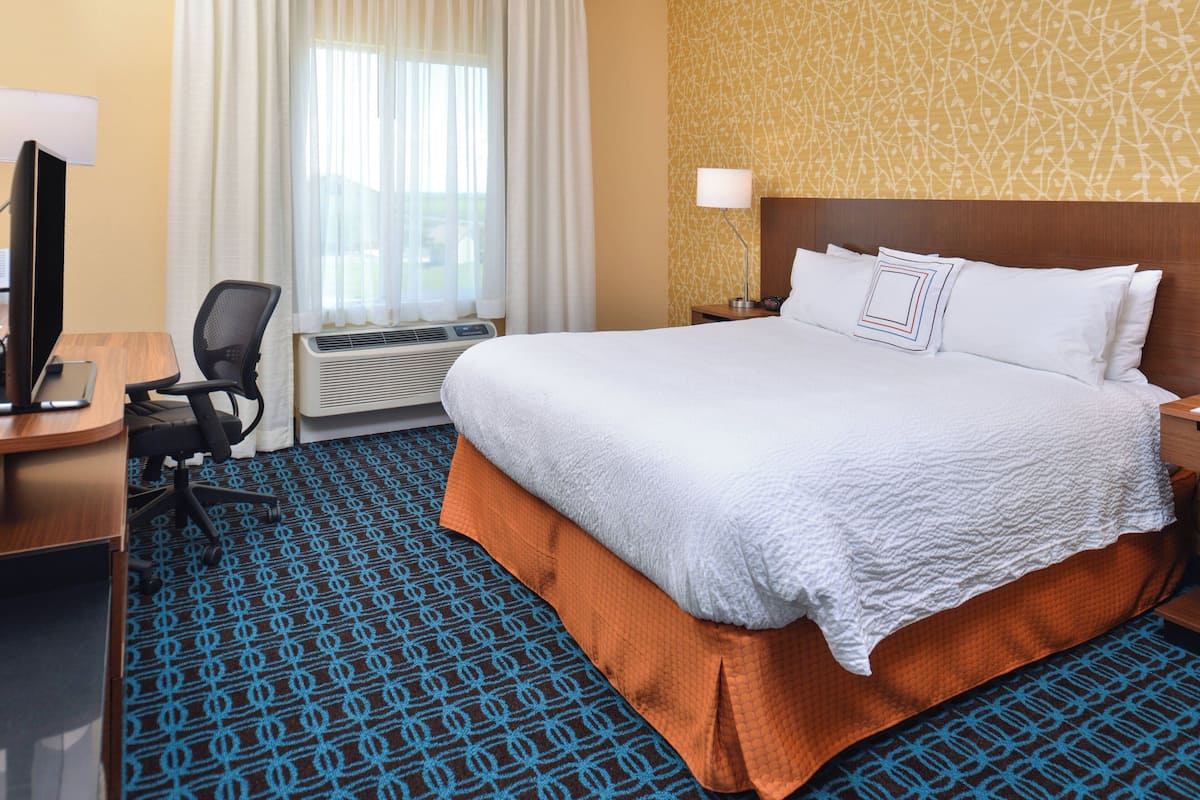 A hotel room with a large bed, a desk with a computer, a chair, and a window with curtains.