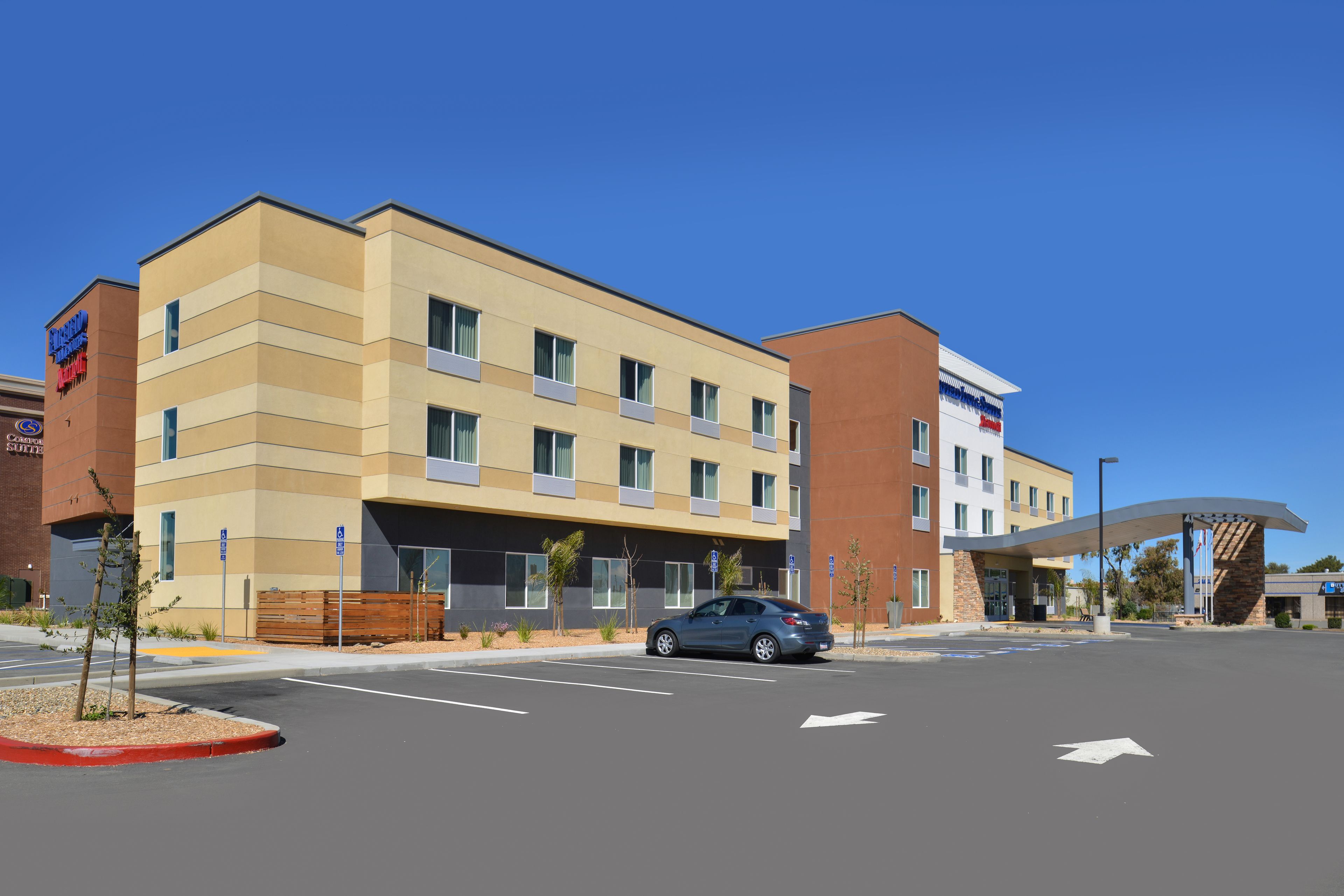Et hotel i flere etager med moderne design, med et fladt tag og en kombination af beige og brune farver på facaden.