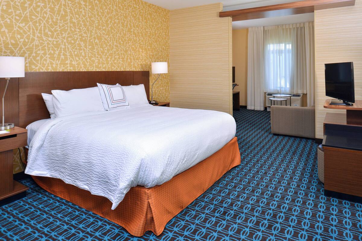 A hotel room with a large bed, a desk with a television, and a small table with a chair.