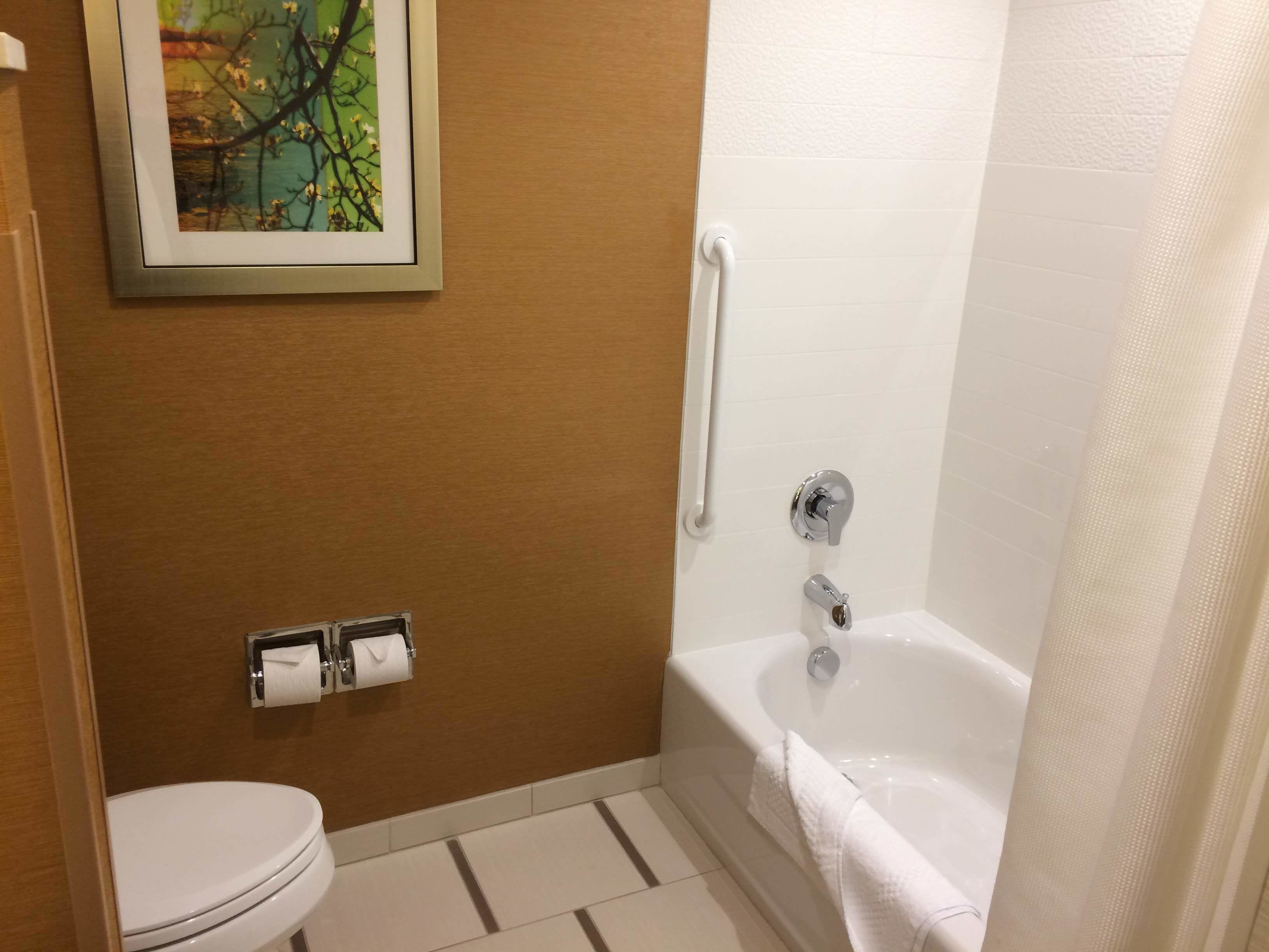 A bathroom with a toilet, a sink with a towel dispenser, and a bathtub with a shower curtain.
