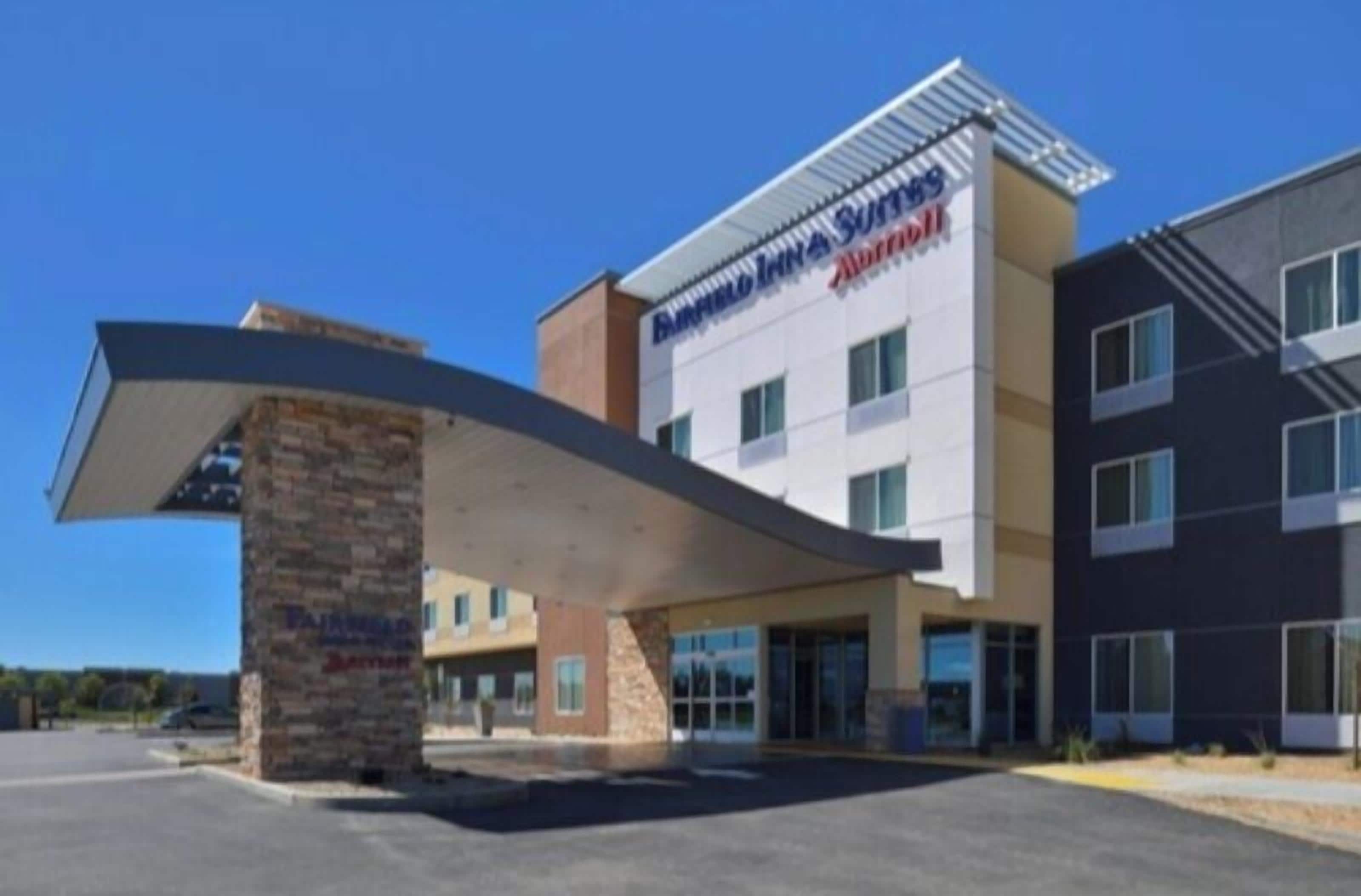 Un hôtel moderne doté d’un auvent imposant à l’entrée, d’une enseigne indiquant « Buffalo Inn Suites » et d’un espace de stationnement bien visible.