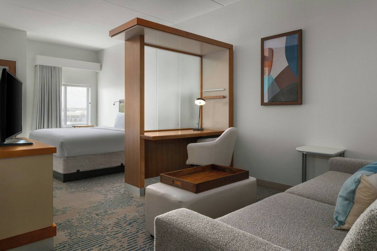 A hotel room with a bed, a desk with a chair, a TV, and a small table.