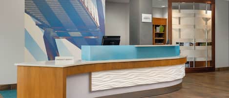 Un mostrador de recepción de hotel con una encimera azul, una placa con nombre blanca y una obra de arte moderna y abstracta en la pared.