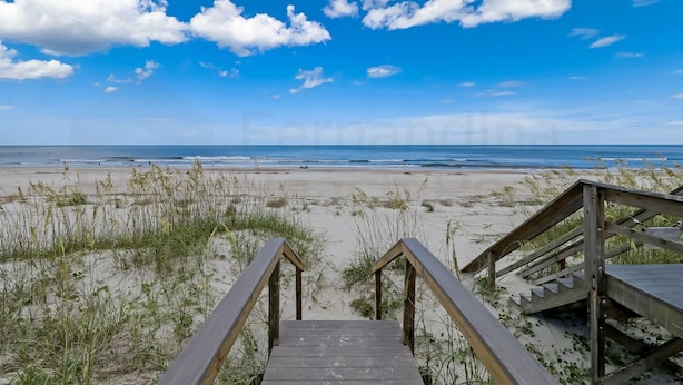 Una escalera de madera que conduce a una playa con cielo despejado y océano al fondo.