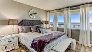 A bedroom with a bed, bedside tables, a mirror, and a view of the sea.
