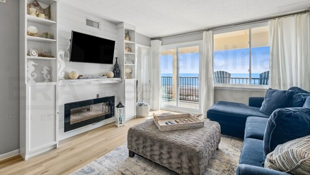 A modern living room with a fireplace, a large TV, and a view of the ocean.