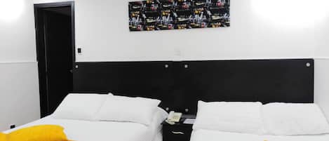 Habitación de hotel con dos camas, cada una con sábanas blancas y almohadas amarillas. Tiene un cabecero negro, una obra de arte en la pared y una puerta a la izquierda.