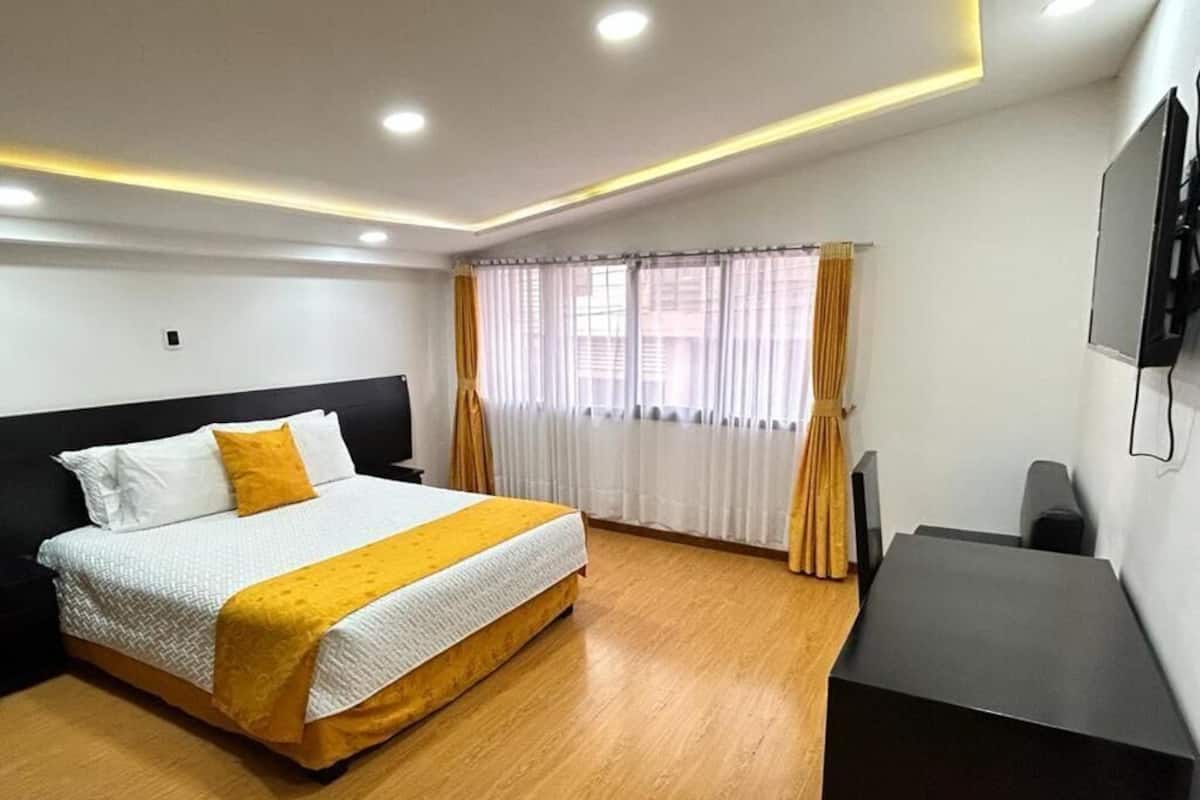 A hotel room with a bed, a desk, a television, and a window with curtains.
