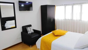 A hotel room with a bed, a black armchair, a wardrobe, a television, and a window with curtains. - Hotel Lagos Latin America (San Juan de Pasto)