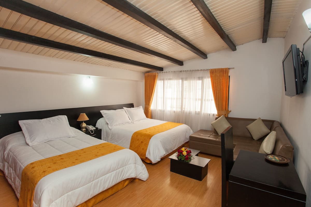 A hotel room with two beds, a sofa, a TV, and a coffee table.