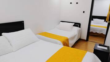 A hotel room with two beds, each with white bedding and a yellow accent. There is a mirror on the wall and a small table with a lamp.