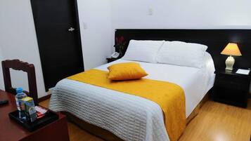 A neatly arranged hotel room with a bed, a bedside table with a lamp, a chair, and a small desk with a water bottle and tissues.