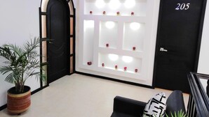 A reception area with a black door marked 205, a white wall with shelves containing small decorative items, and a potted plant. - Hotel Lagos Latin America (San Juan de Pasto)