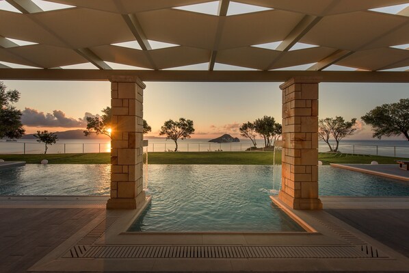 A pool area with a sunset view, surrounded by stone pillars and a glass ceiling.