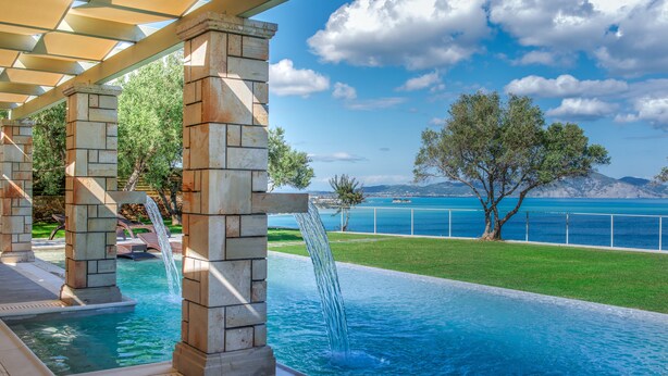 A pool area with a waterfall feature, a pergola, and a view of the sea and mountains.