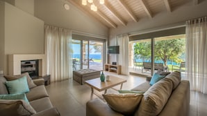 A spacious living room with a fireplace, comfortable seating, a coffee table, and large windows offering a view of the outdoors.