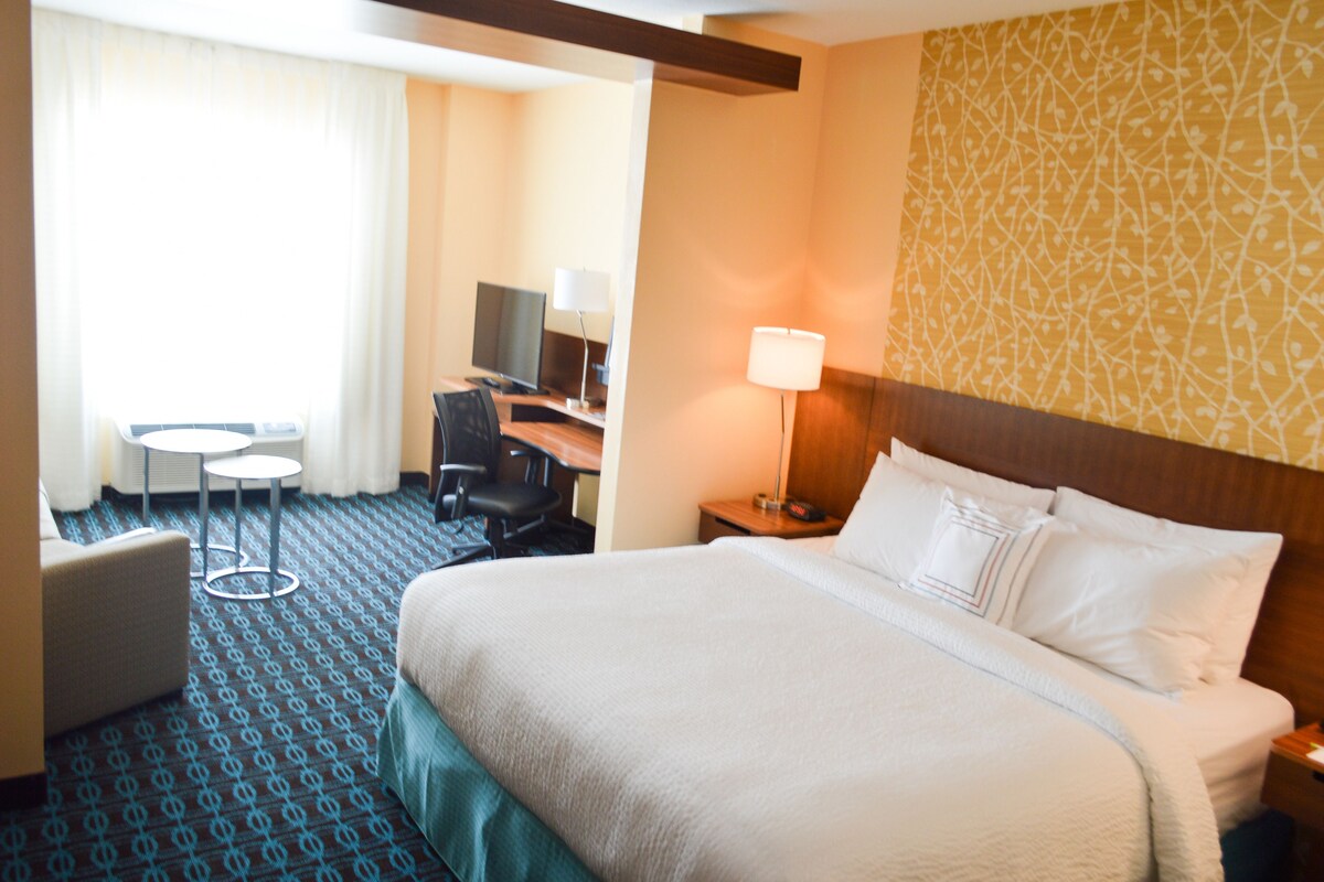 A hotel room with a large bed, a desk with a chair, a television, and a lamp.