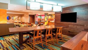 A hotel lobby with a large wooden reception desk, multiple seating areas with tables and chairs, and a flat-screen TV mounted on the wall. - Fairfield Inn & Suites San Antonio Brooks City Base (San Antonio)