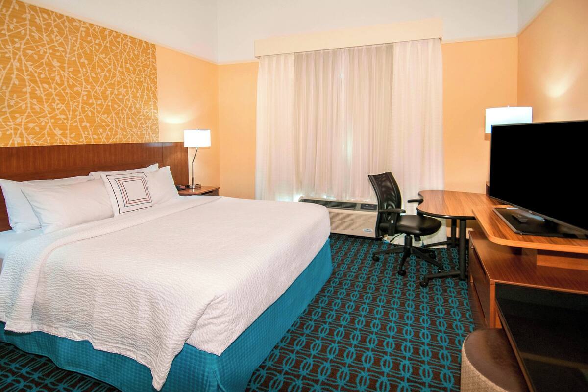A hotel room with a large bed, a desk with a chair, a television, and a window with curtains.