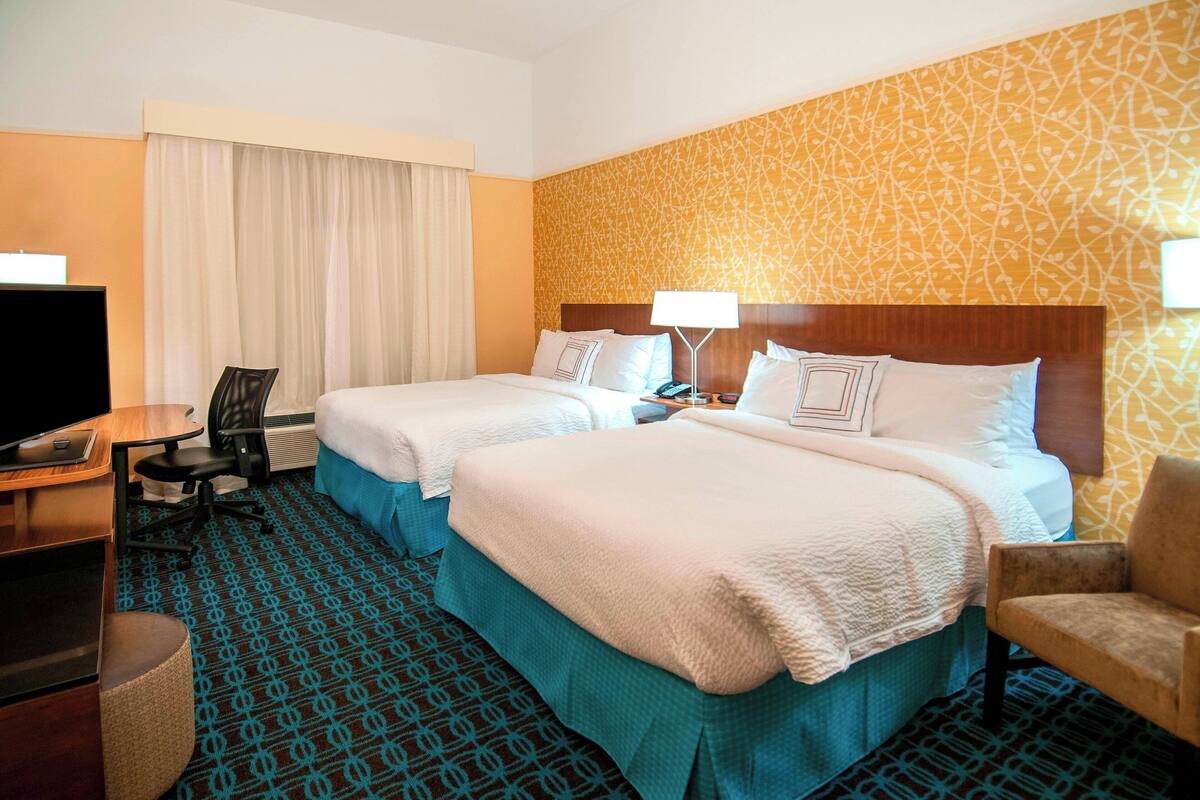 A hotel room with two beds, a desk, a chair, a TV, and a patterned carpet.