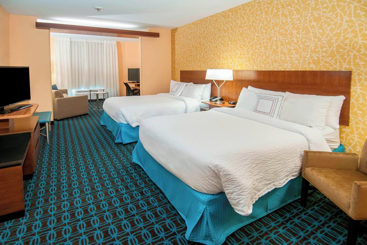 A hotel room with two beds, a desk with a TV, a chair, and a patterned carpet.