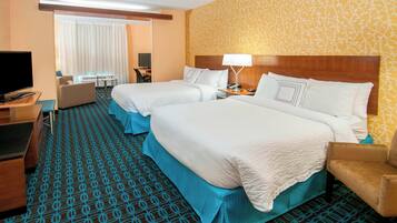 Ein Hotelzimmer mit zwei Betten, einem Schreibtisch mit Fernseher, einem Sessel und einem gemusterten Teppich.