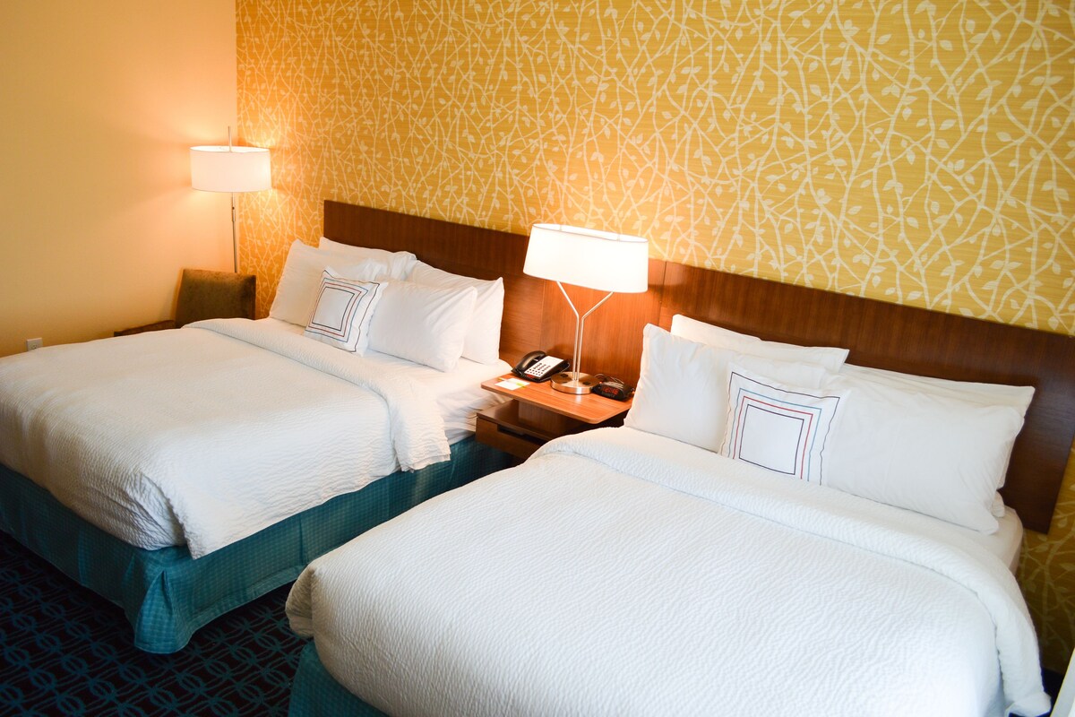 A hotel room with two beds, a nightstand with a lamp, and a patterned wall.