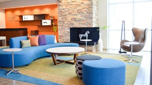 A modern lounge area with a stone wall, blue seating, and a fireplace. - Fairfield Inn & Suites San Antonio Brooks City Base (San Antonio)