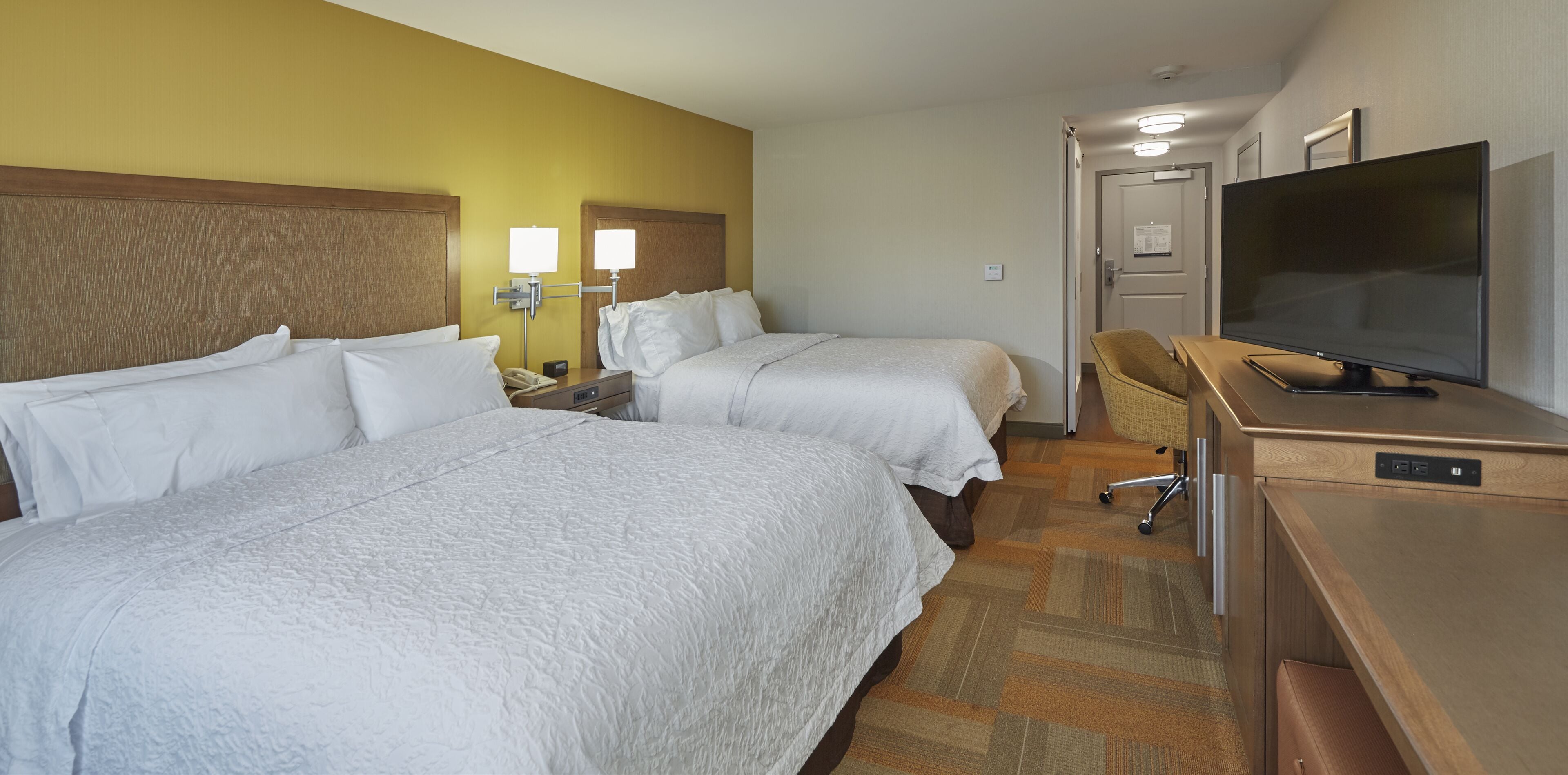 Ein Hotelzimmer mit zwei Betten, einem Schreibtisch, einem Fernseher und einem Sessel.