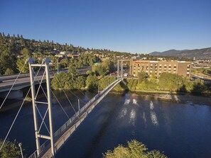 A suspension bridge over a river with a cityscape in the background, including a hotel named "Hampton Inn & Suites."