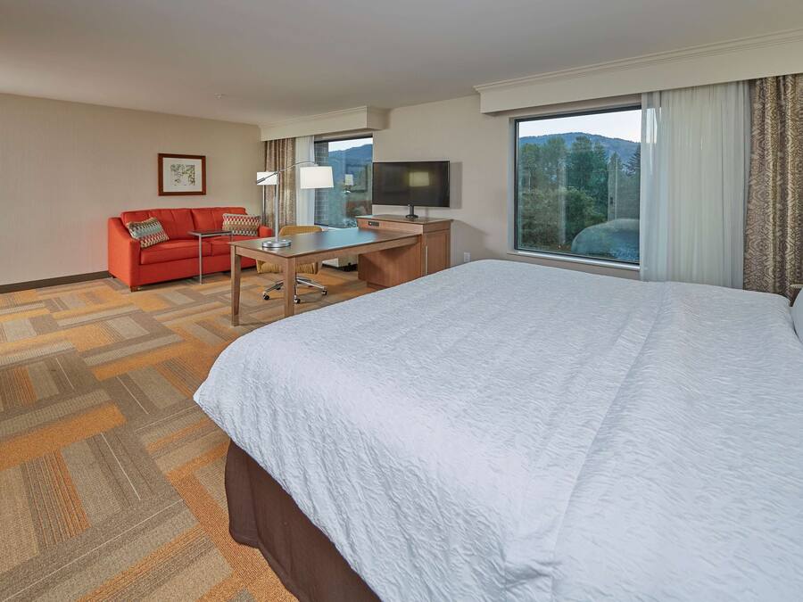 Ein Hotelzimmer mit einem großen Bett, einem Schreibtisch mit Stuhl, einem roten Sofa und einem Fernseher.