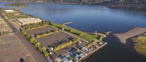 An aerial view of a waterfront property with a parking lot, a dock, and a building with a flat roof.