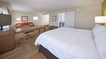 Quarto de hotel com cama, escrivaninha, televisão, sofá e banheiro visível por uma porta aberta.