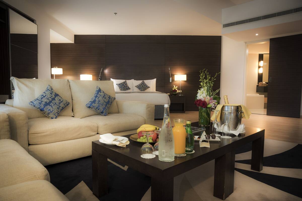 A modern hotel room with a sofa, a dining table, a bed, and a minibar.