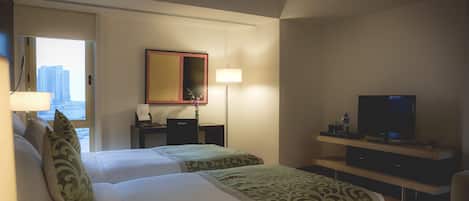 Habitación de hotel con dos camas, un escritorio, un televisor y una ventana con vista a la ciudad.