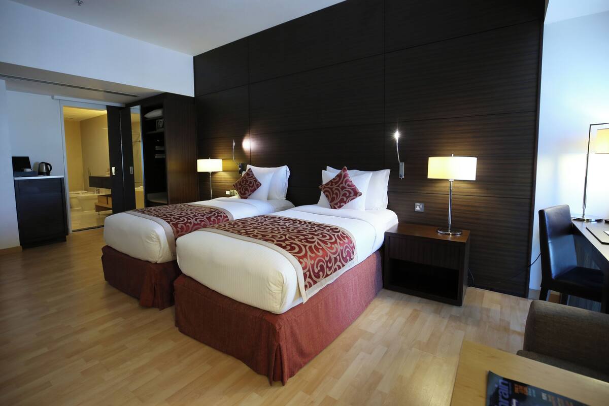 A hotel room with two beds, a desk, and a chair.