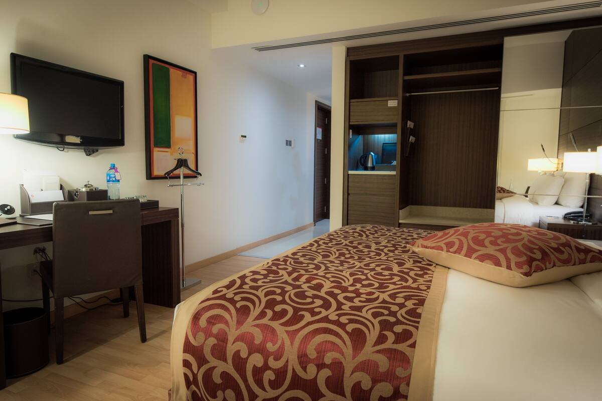 A hotel room with a bed, a desk, a chair, a television, and a wardrobe.