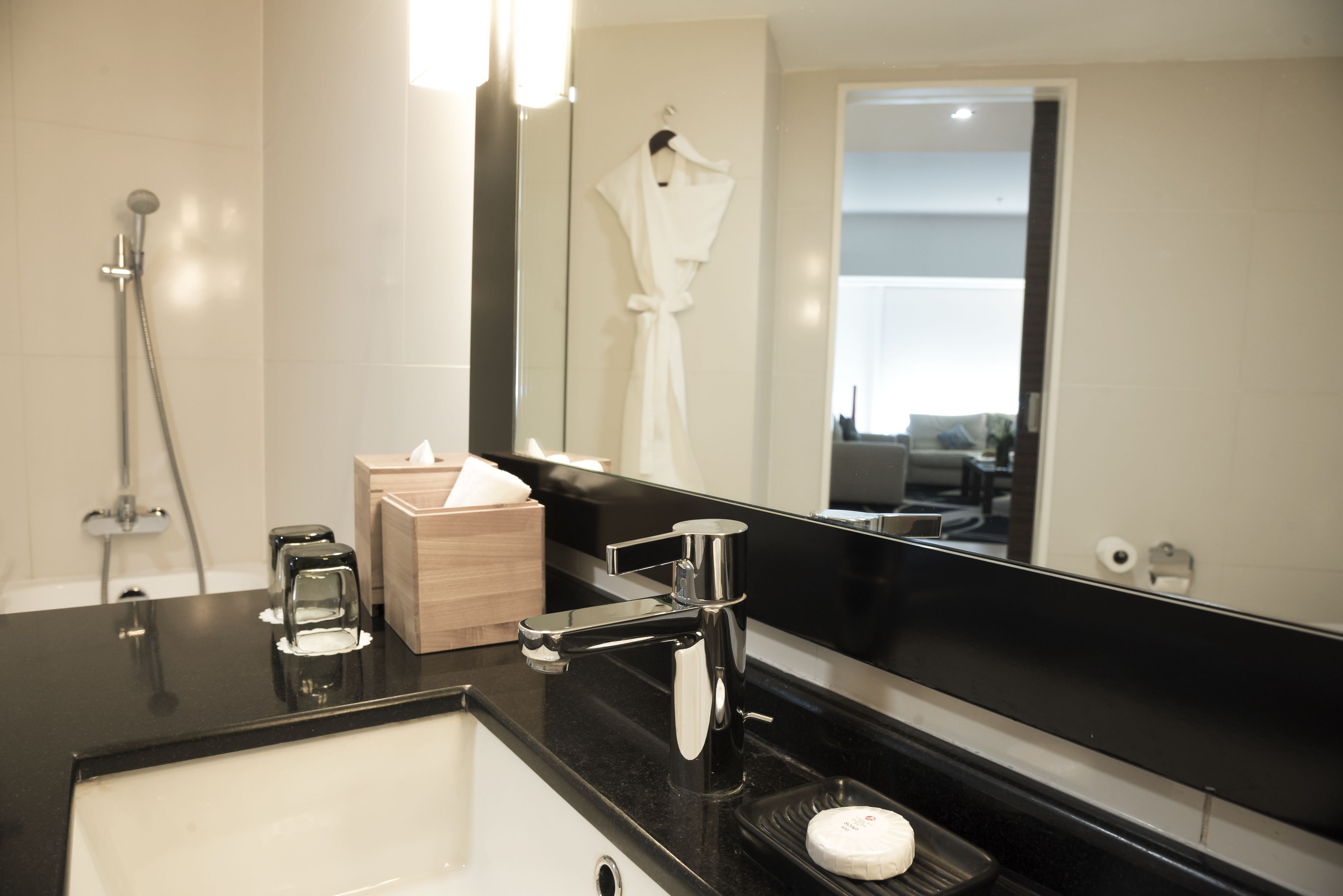 A modern bathroom with a black countertop, a white sink, a large mirror, a towel rack, and a shower area.