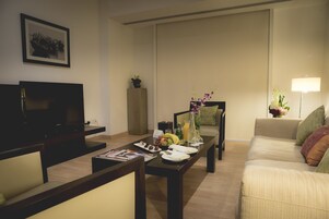 Una sala de estar con una televisión de pantalla plana, una mesa de centro con frutas y un florero, un sofá y una lámpara.