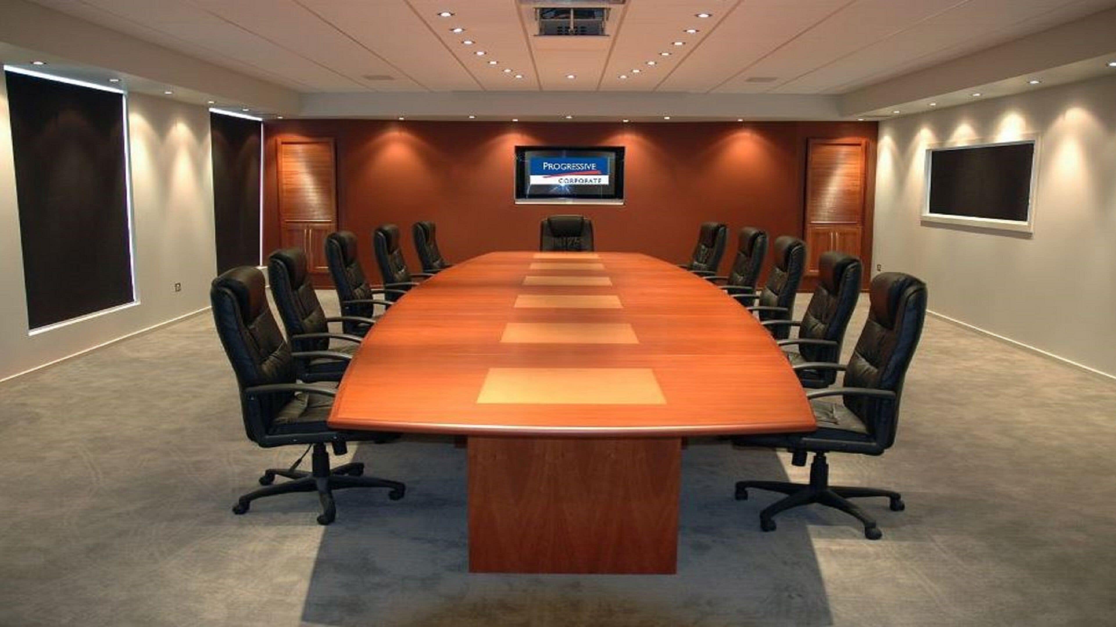 A conference room with a long table, black chairs, and a television screen displaying 'Progressive Corporate'.