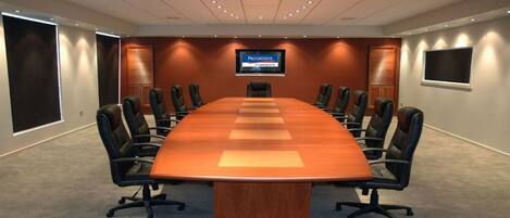 A conference room with a long table, black chairs, and a television screen displaying 'Progressive Corporate'.