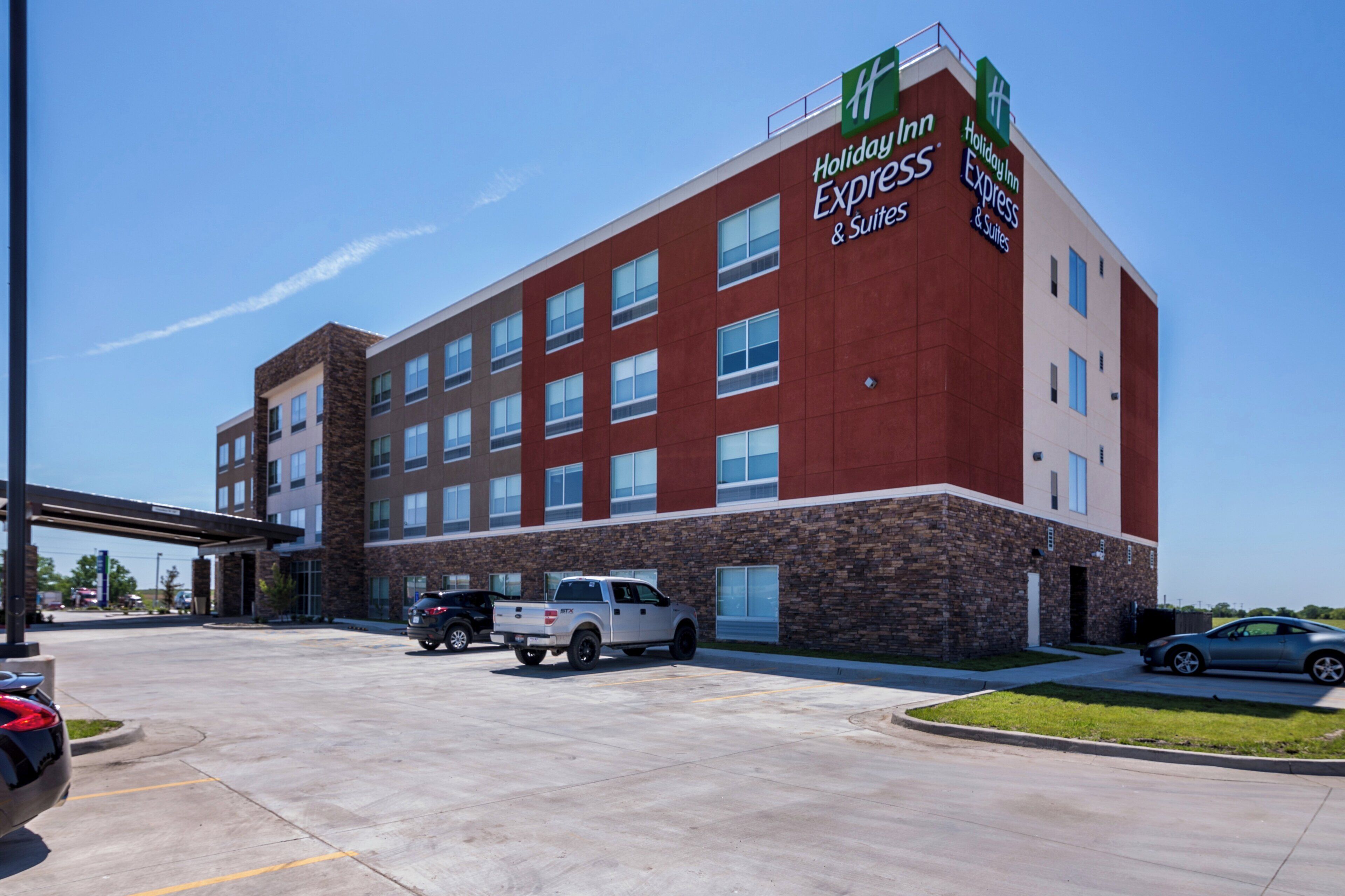 Un hotel Holiday Inn Express & Suites con fachada de ladrillo, múltiples ventanas y un estacionamiento con vehículos.
