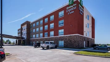 Un hotel Holiday Inn Express & Suites con fachada de ladrillo, múltiples ventanas y un estacionamiento con vehículos.