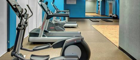 A gym with multiple treadmills, a mirrored wall, and exercise balls.
