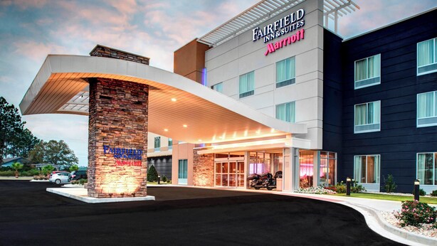 Een Fairfield Inn & Suites Marriott hotel met een moderne ingang, een stenen zuil en een parkeerplaats.
