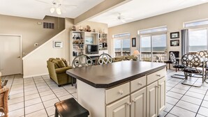 A spacious kitchen with a large island, a dining area with chairs, a sofa, and a staircase leading to another level. - 812 S. Fletcher - 3 Br Cottage (Fernandina Beach)