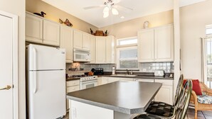 A kitchen with white cabinets, a refrigerator, a microwave, a stove, and a dining area with a chair and table. - 812 S. Fletcher - 3 Br Cottage (Fernandina Beach)