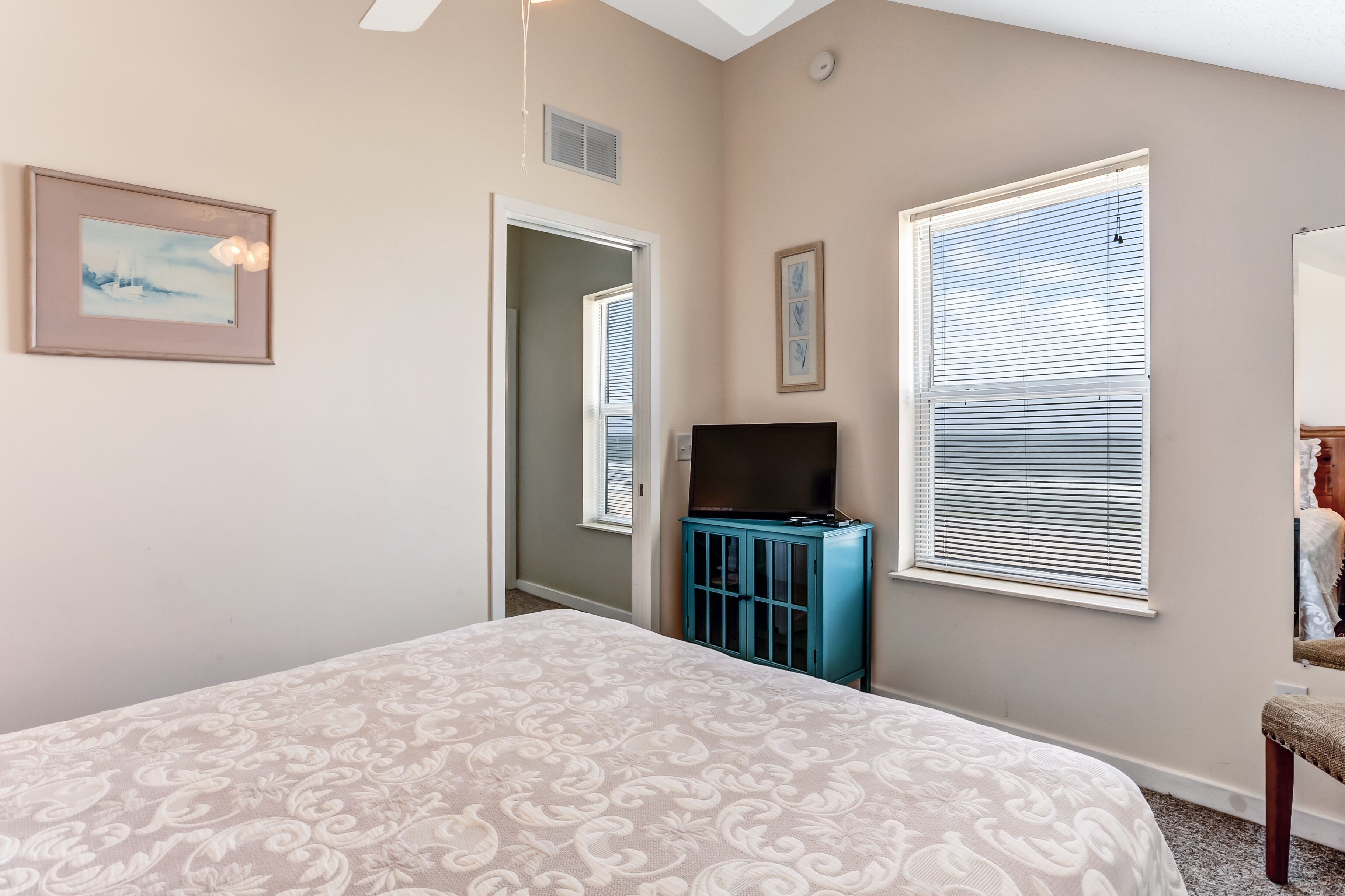 A bedroom with a bed, a television on a blue cabinet, and a window with blinds.