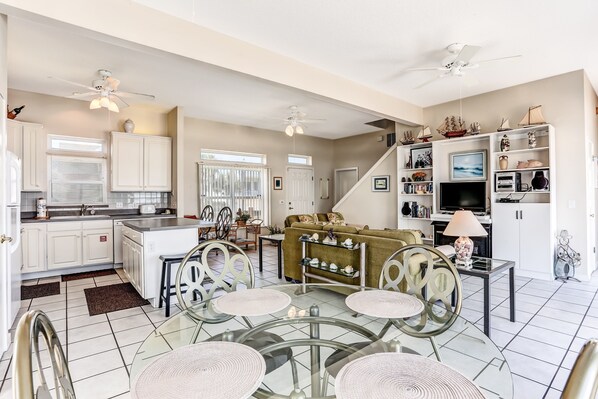 A spacious living area with a glass dining table, a sofa, and a kitchen in the background. - 812 S. Fletcher - 3 Br Cottage (Fernandina Beach)